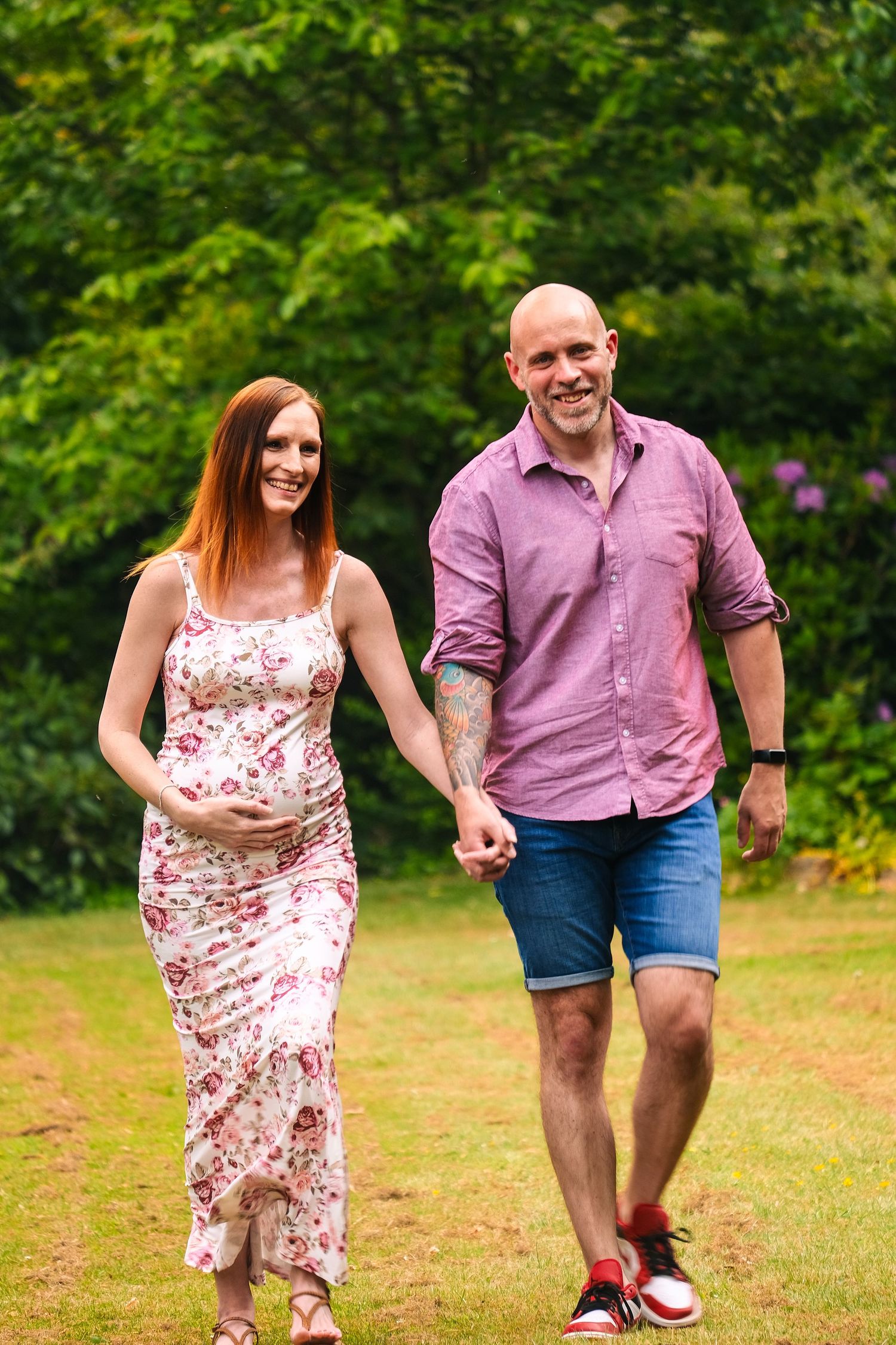 Playful couple running and posing together on a grassy lawn during their maternity shoot.