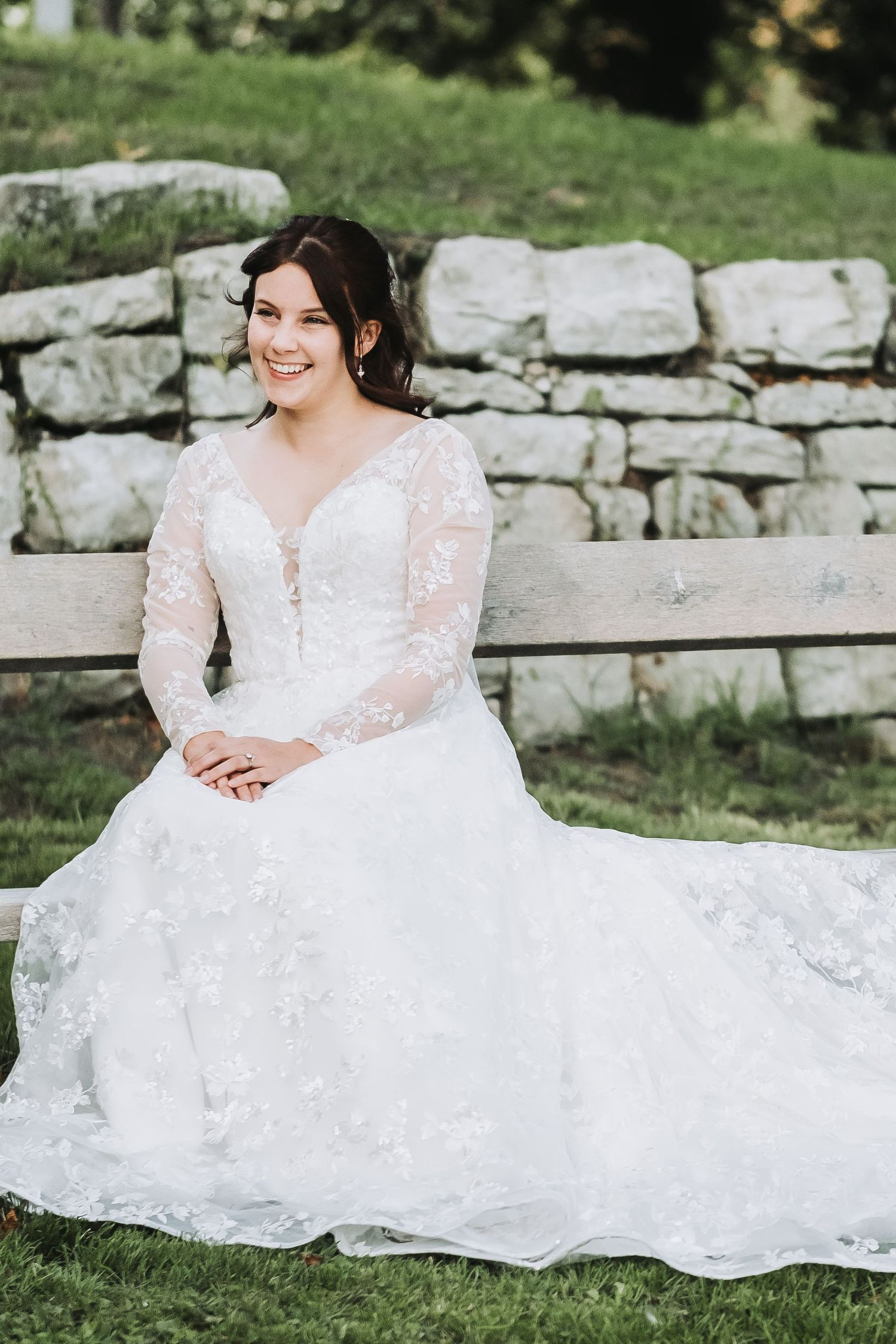 A white lace wedding dress with long sleeves spreads elegantly across stone steps in an outdoor setting.