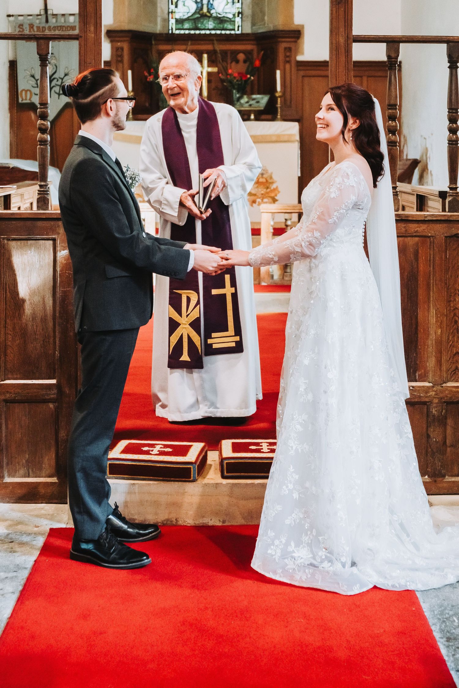A couple dances joyfully during their wedding ceremony on a red carpet in a traditional church setting.