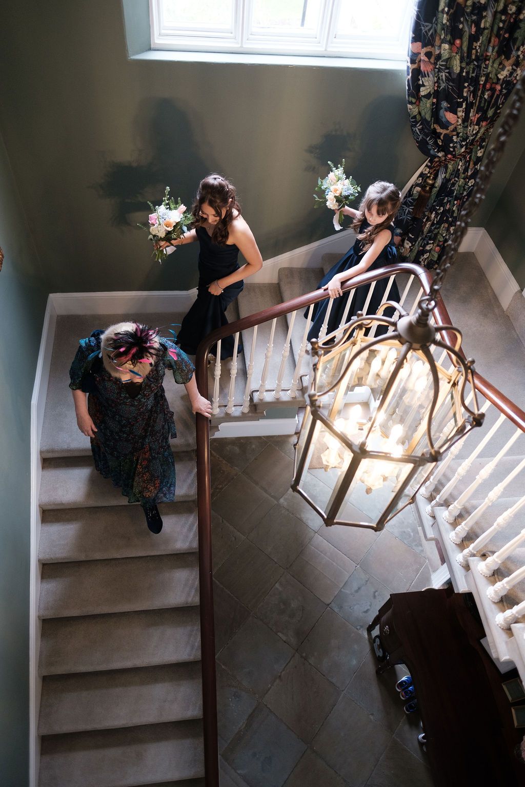 Mother of bride in a floral headpiece walking down the staircase past the hanging lantern