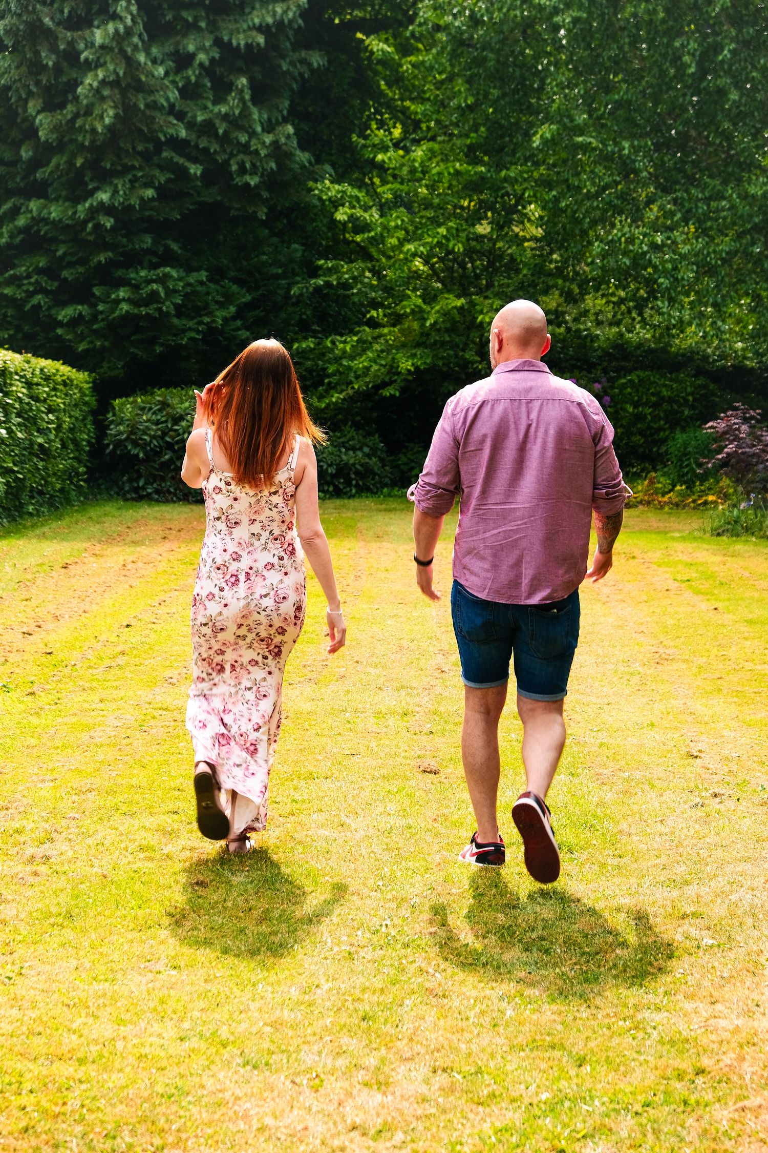 Two people strolling through a grassy meadow surrounded by trees on a bright summer day.