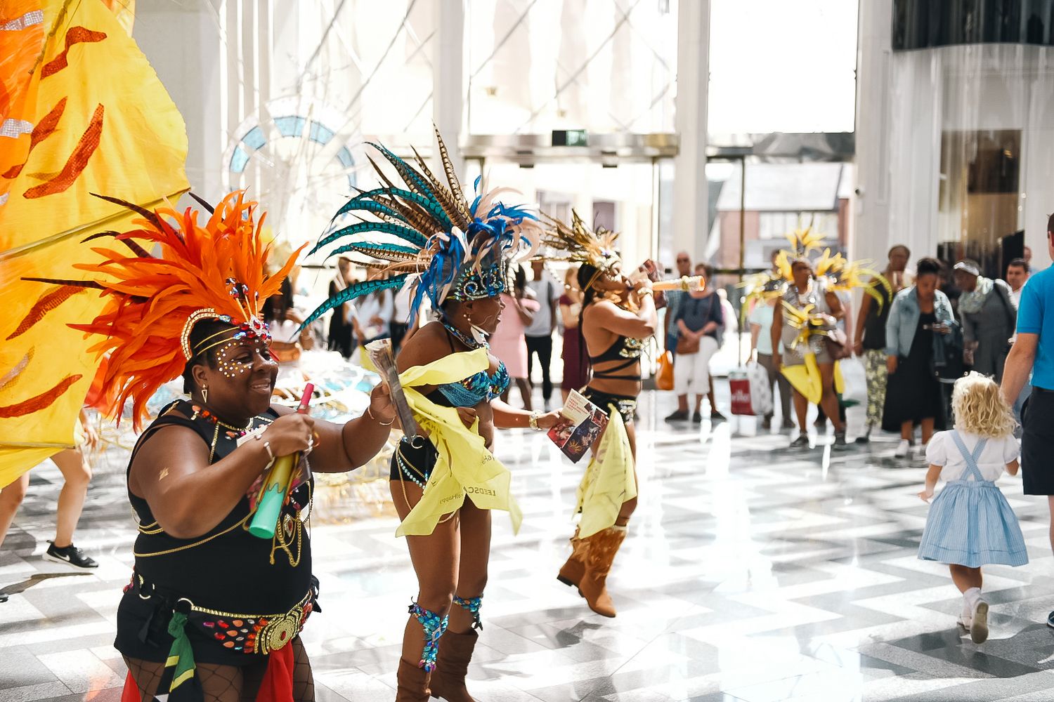 Carnival performers in bright feathered costumes entertaining crowd in indoor venue shot in Leeds by 21 Photography