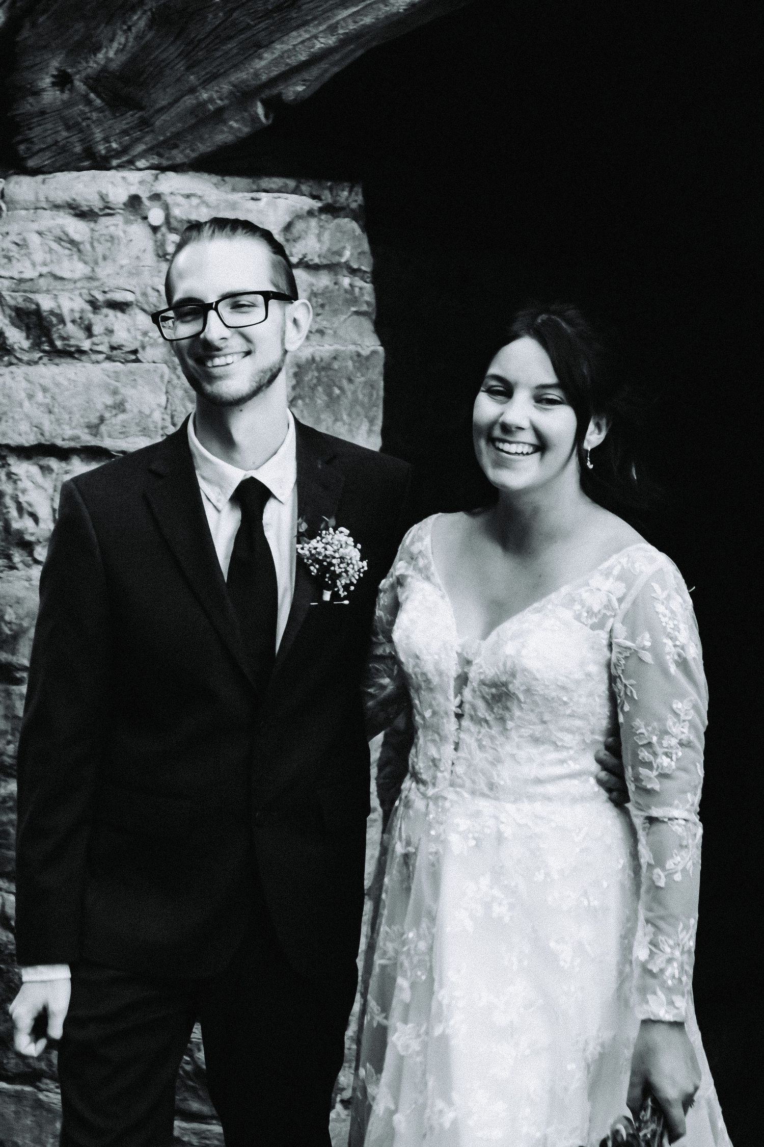 A happy couple shares candid moments in black and white wedding photos against a stone wall backdrop.