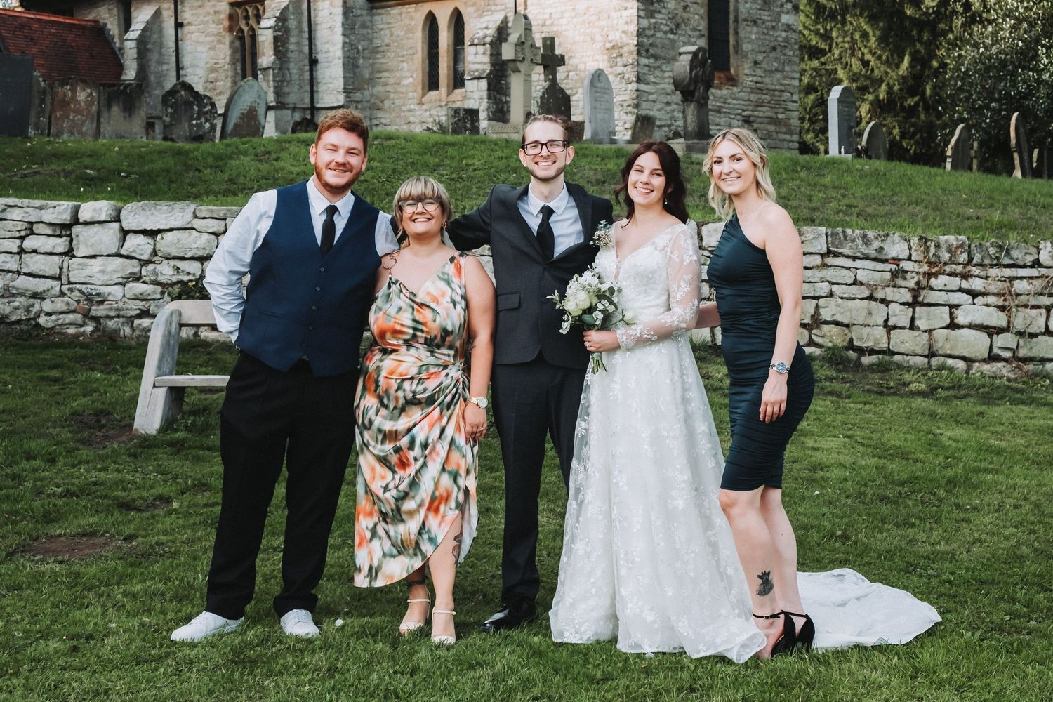 Wedding celebration with guests mingling on a grassy lawn near stone walls.