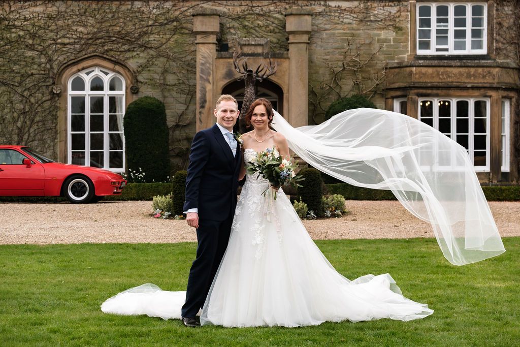 Bride's veil caught in the wind in front of Dunston Hall with a red porsche 944 parked nearby
