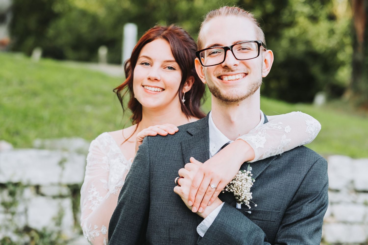 A happy couple embraces outdoors during a wedding photoshoot in a lush garden setting.