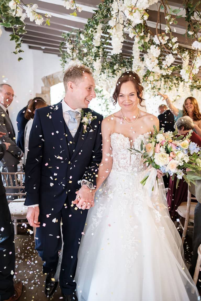 Bride and groom walk down the aisle smiling as confetti falls around them at Dunston Hall Estate taken by 21 Photography