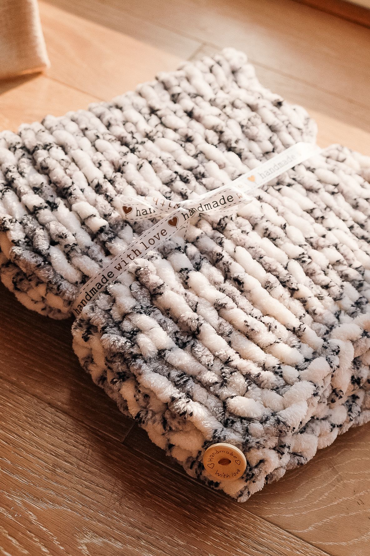 Cozy knitted blanket in white and grey chunky yarn with wooden button detail on wooden floor shot in Chesterfield by 21 Photography