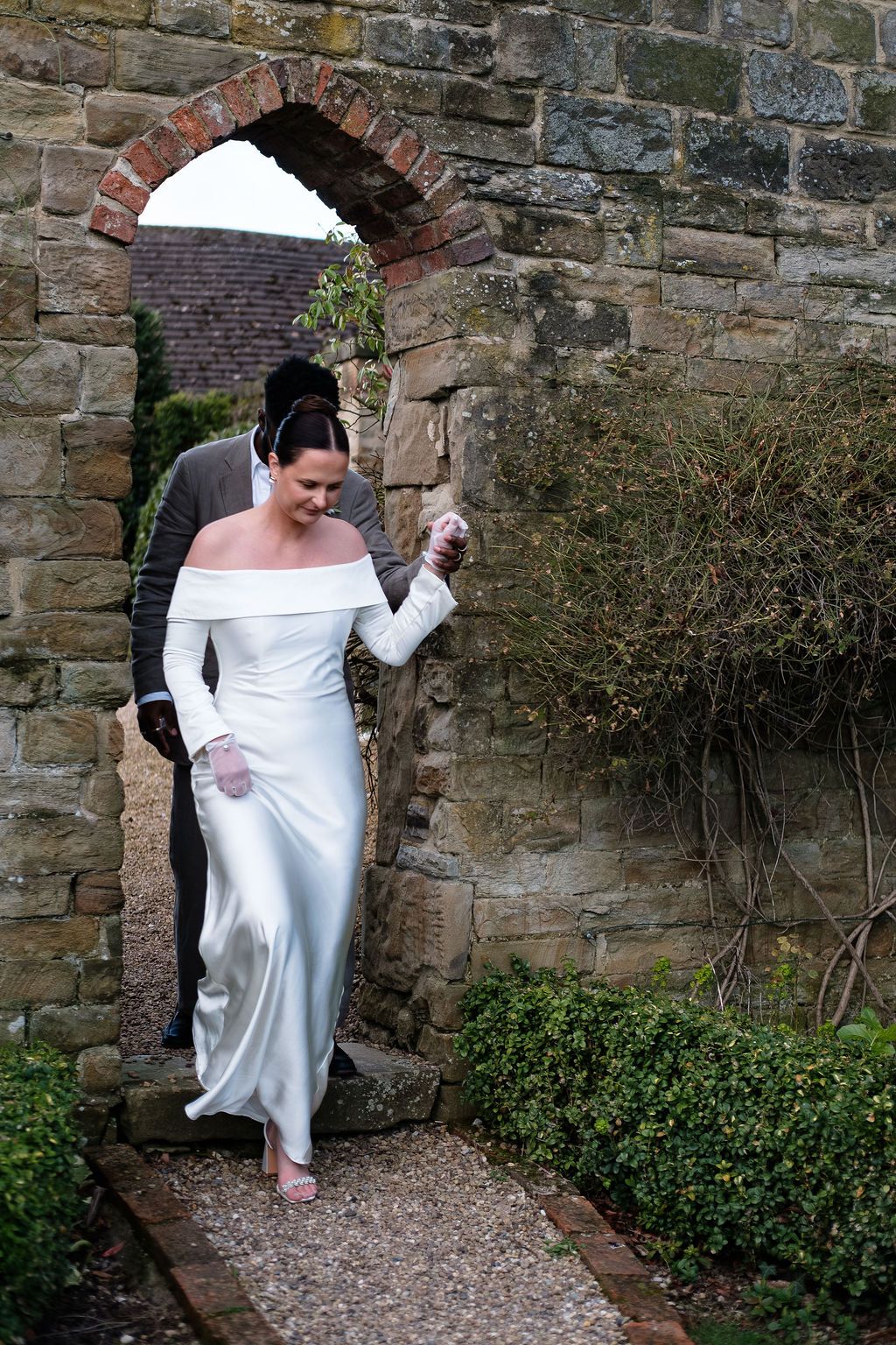 Bride's dress and veil disappearing through a stone garden archway