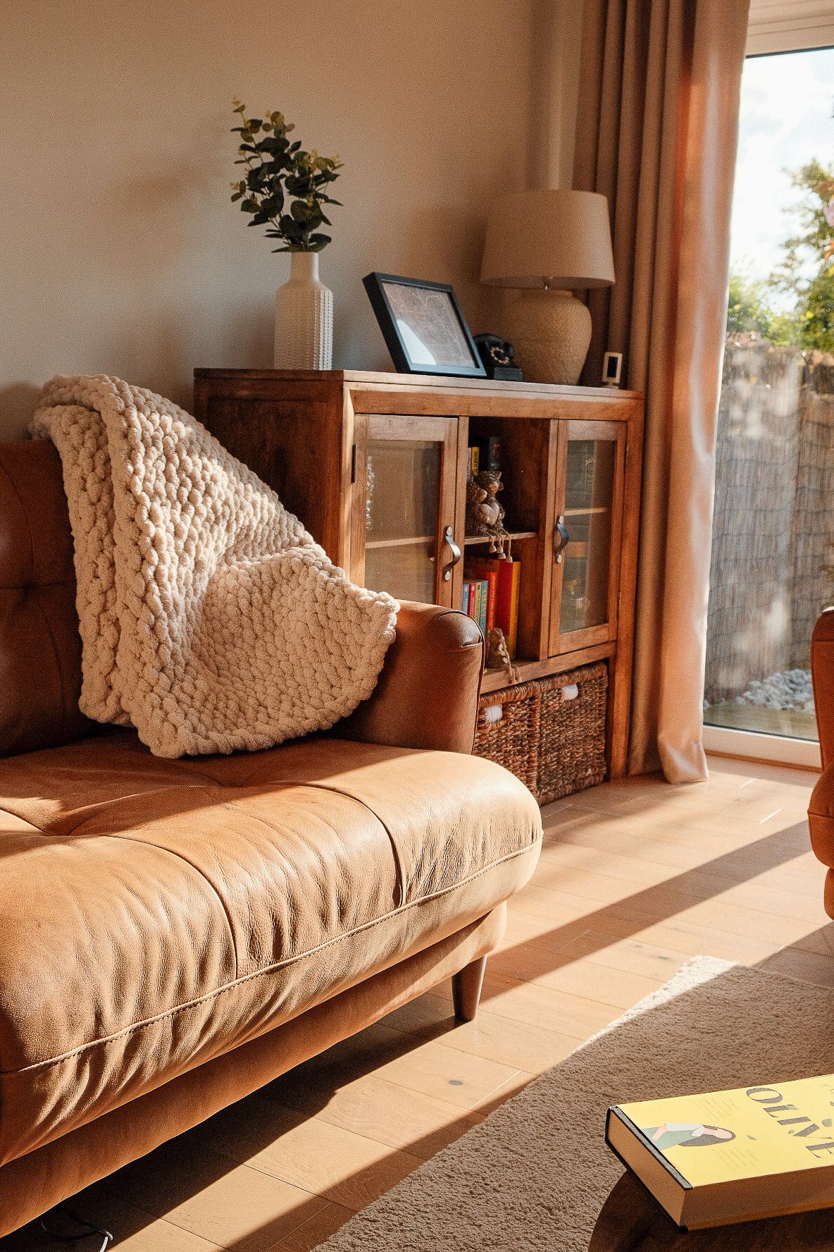 Cozy living room with cream blanket on couch and sunlight streaming through window.