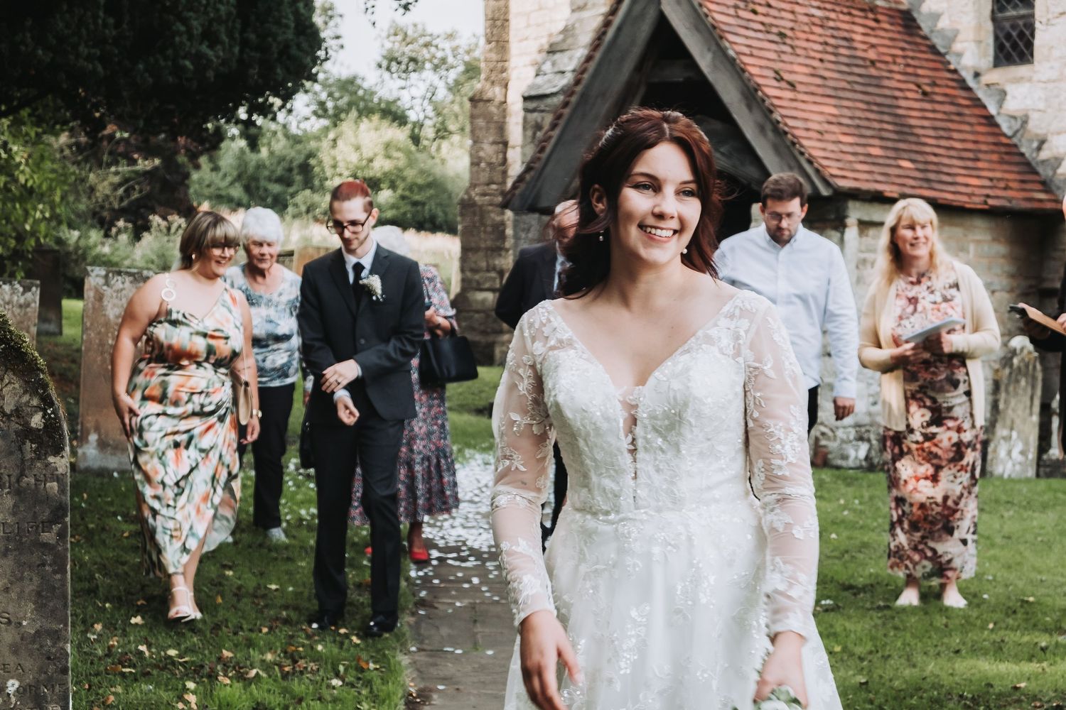 Wedding party gathering outdoors on a sunny day near a historic stone building.