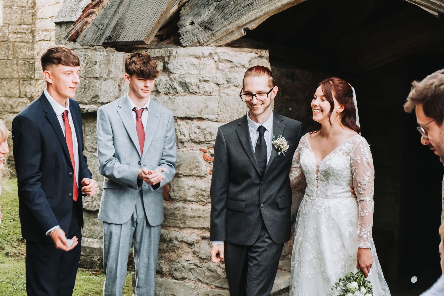 A joyful wedding party gathers outside a rustic stone church entrance during a celebration.
