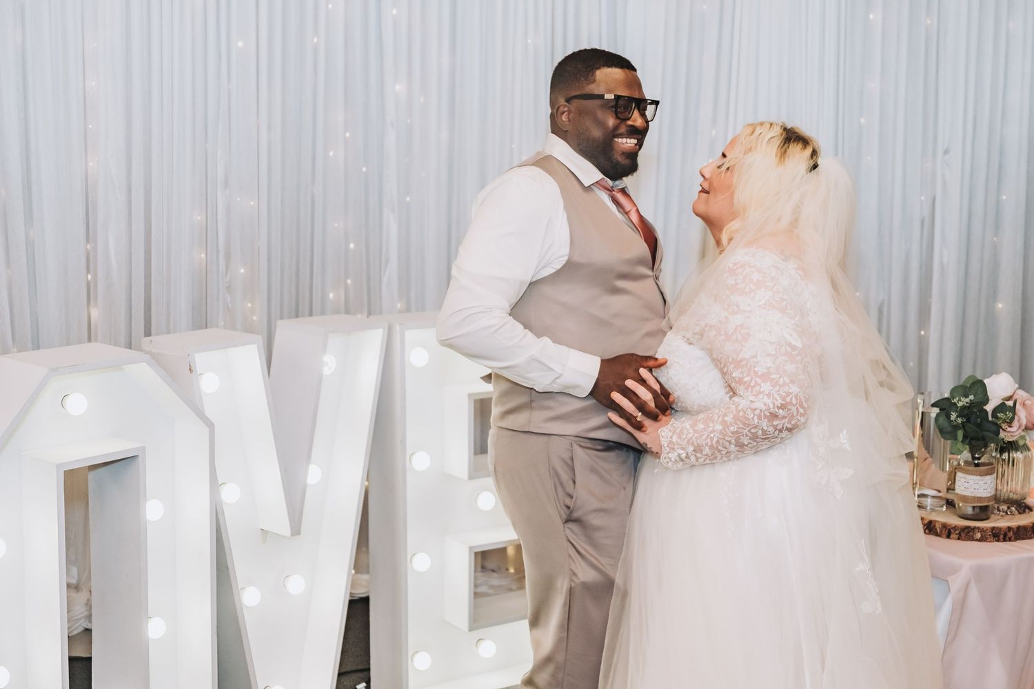 A romantic wedding dance moment at a reception with the couple embraced in matching white outfits.