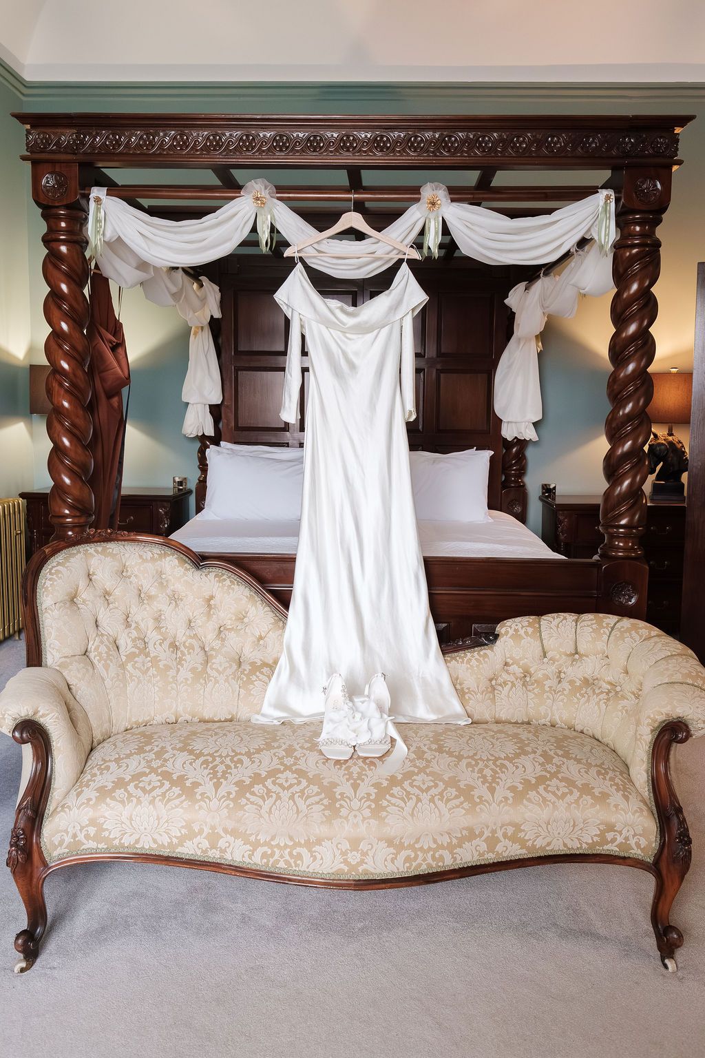 Wedding dress hanging from a four poster bed with white drapes