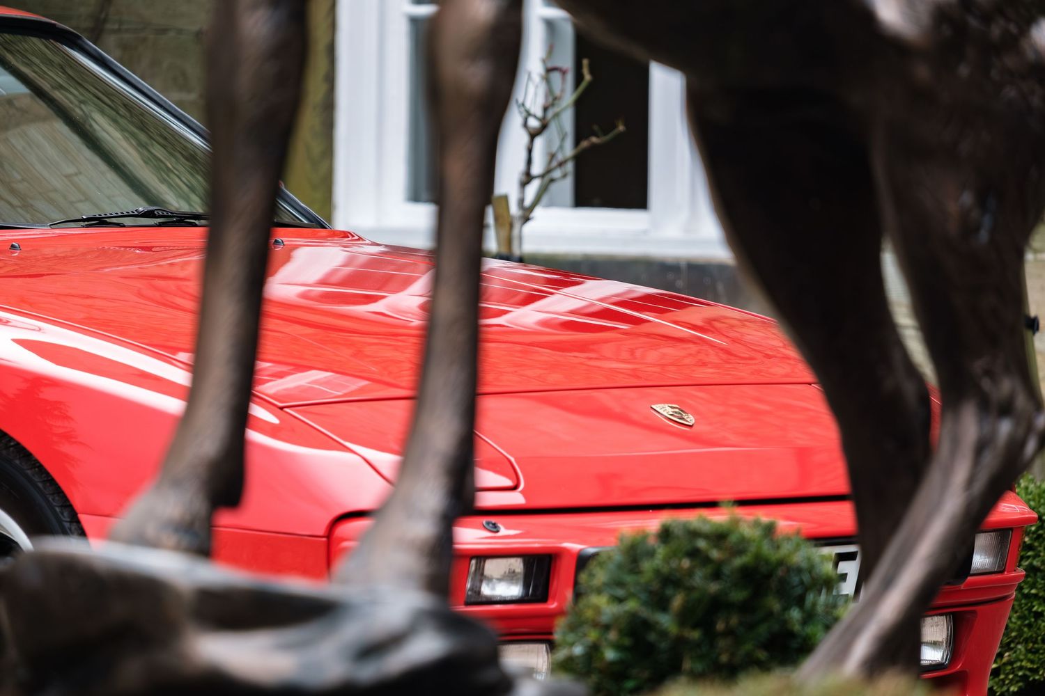 Red Ferrari sports car parked in a driveway, viewed through bronze horse sculpture legs.