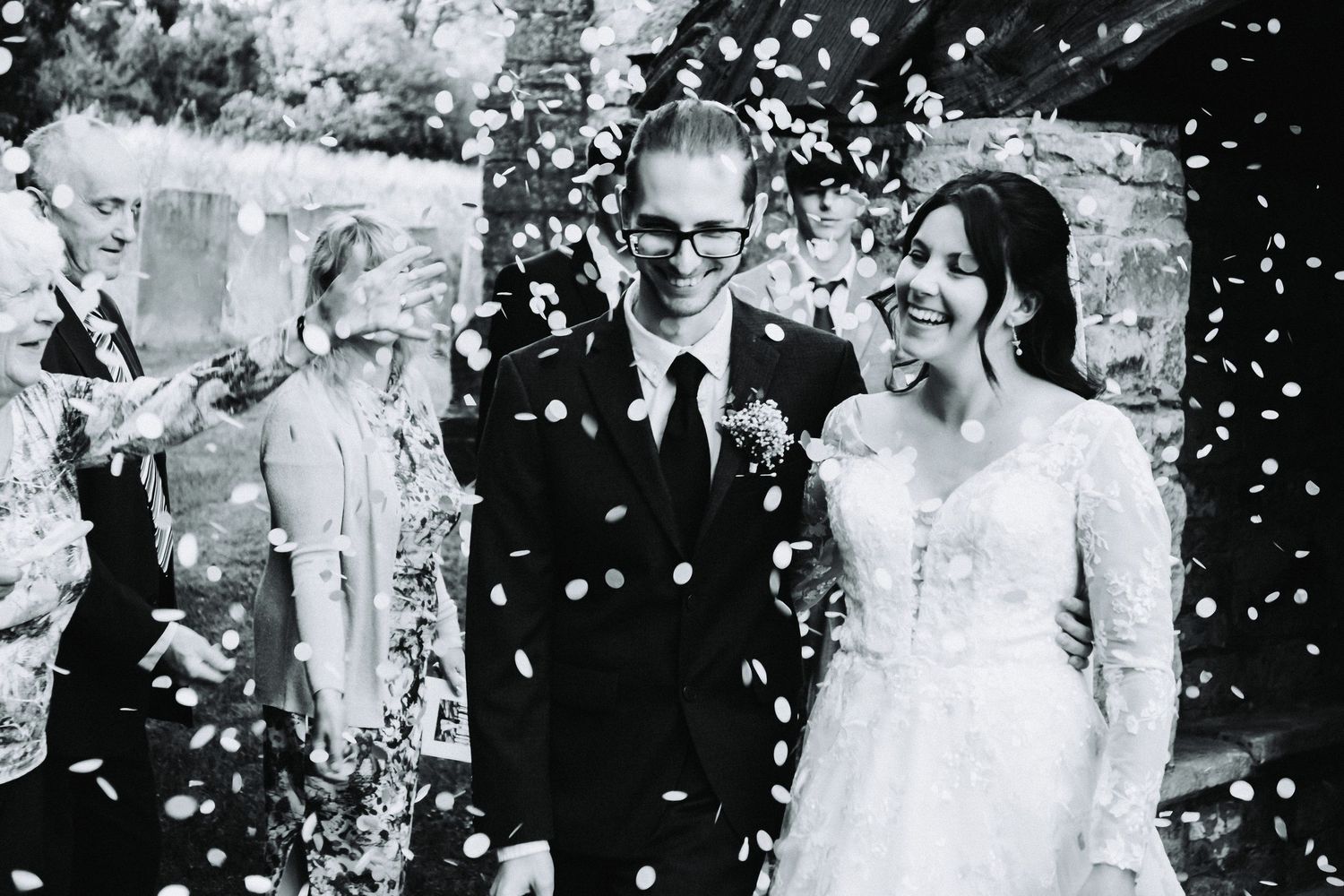 A joyful wedding celebration with confetti falling around the newlyweds in black and white photography.