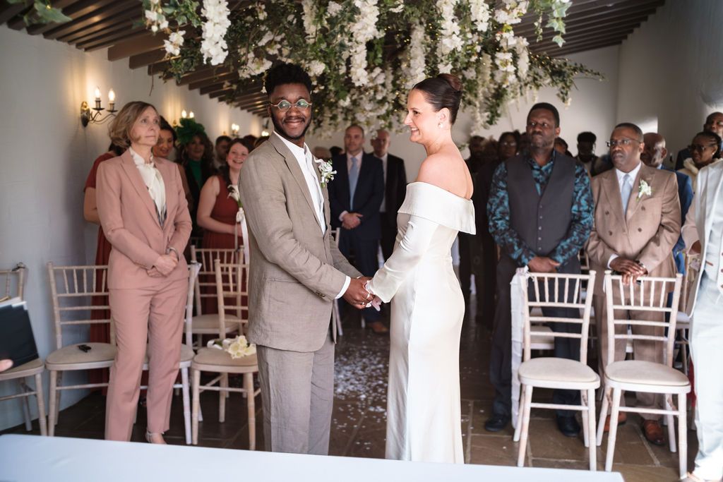 Groom holding the bride's hand during the ceremony vows, guests seated either side