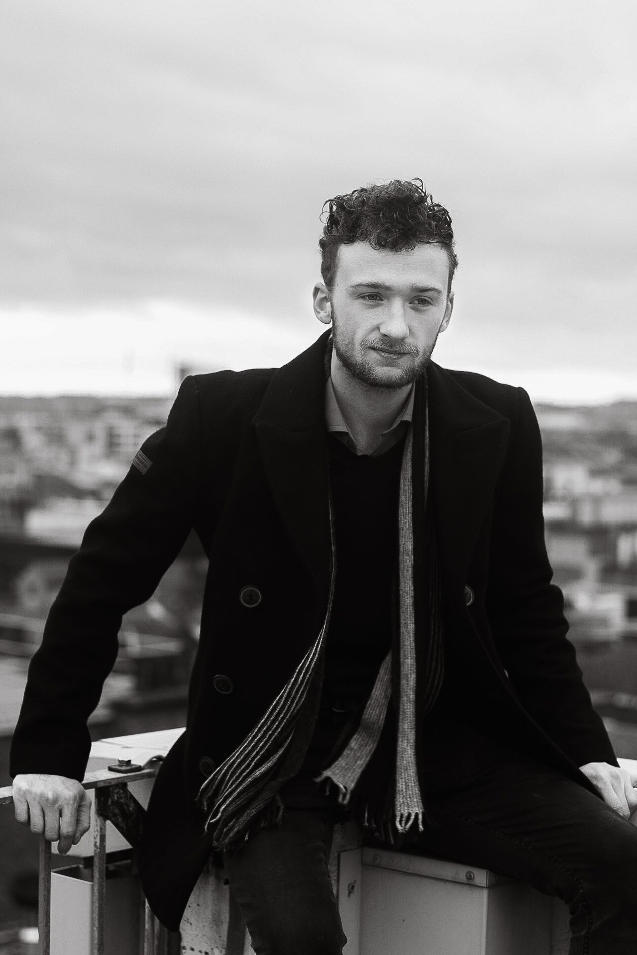 Series of black and white portraits showing someone in a black coat and scarf against an urban background.
