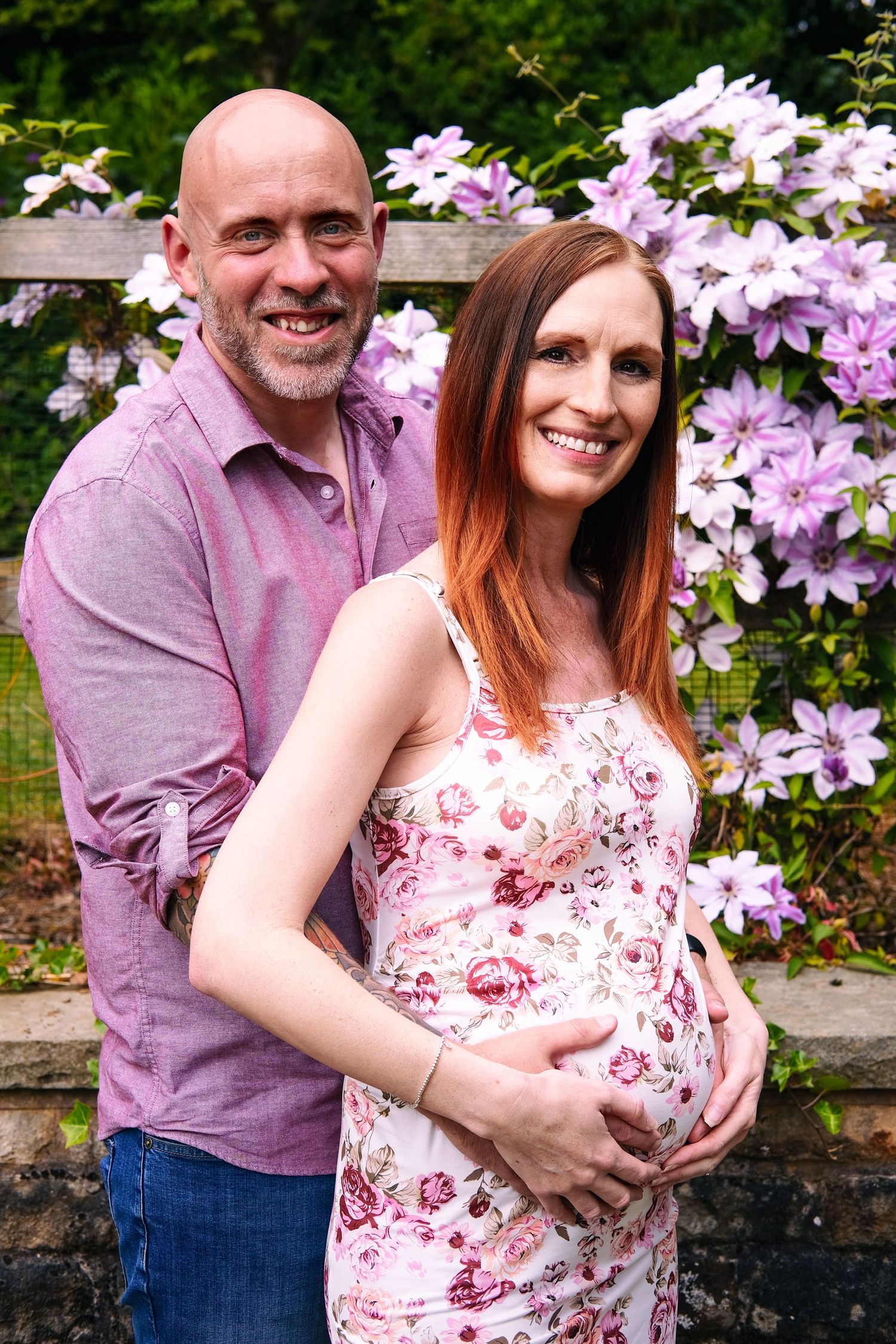 Couple posing by purple clematis flowers, wearing matching purple tones.