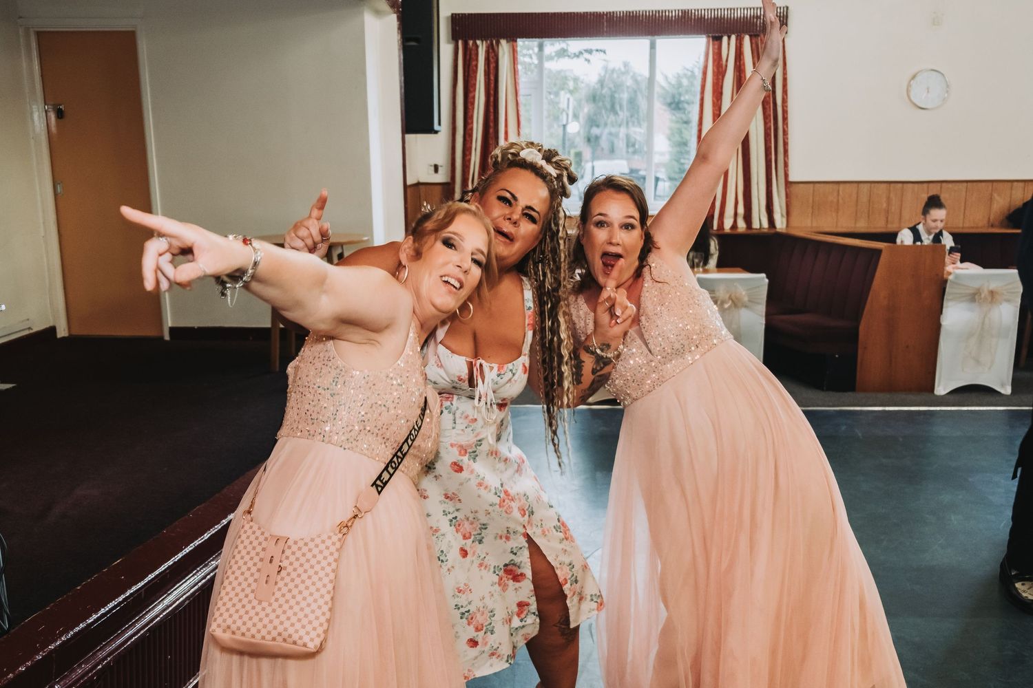 A group in peach-colored dresses dances and celebrates together in an indoor venue.