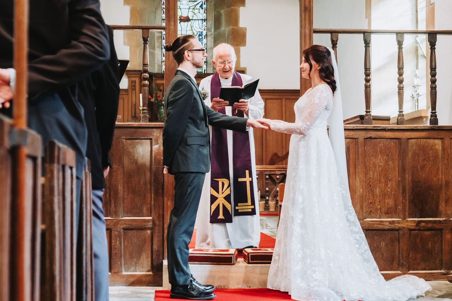 Traditional church wedding ceremony with wooden pews and red carpet aisle in elegant interior setting.