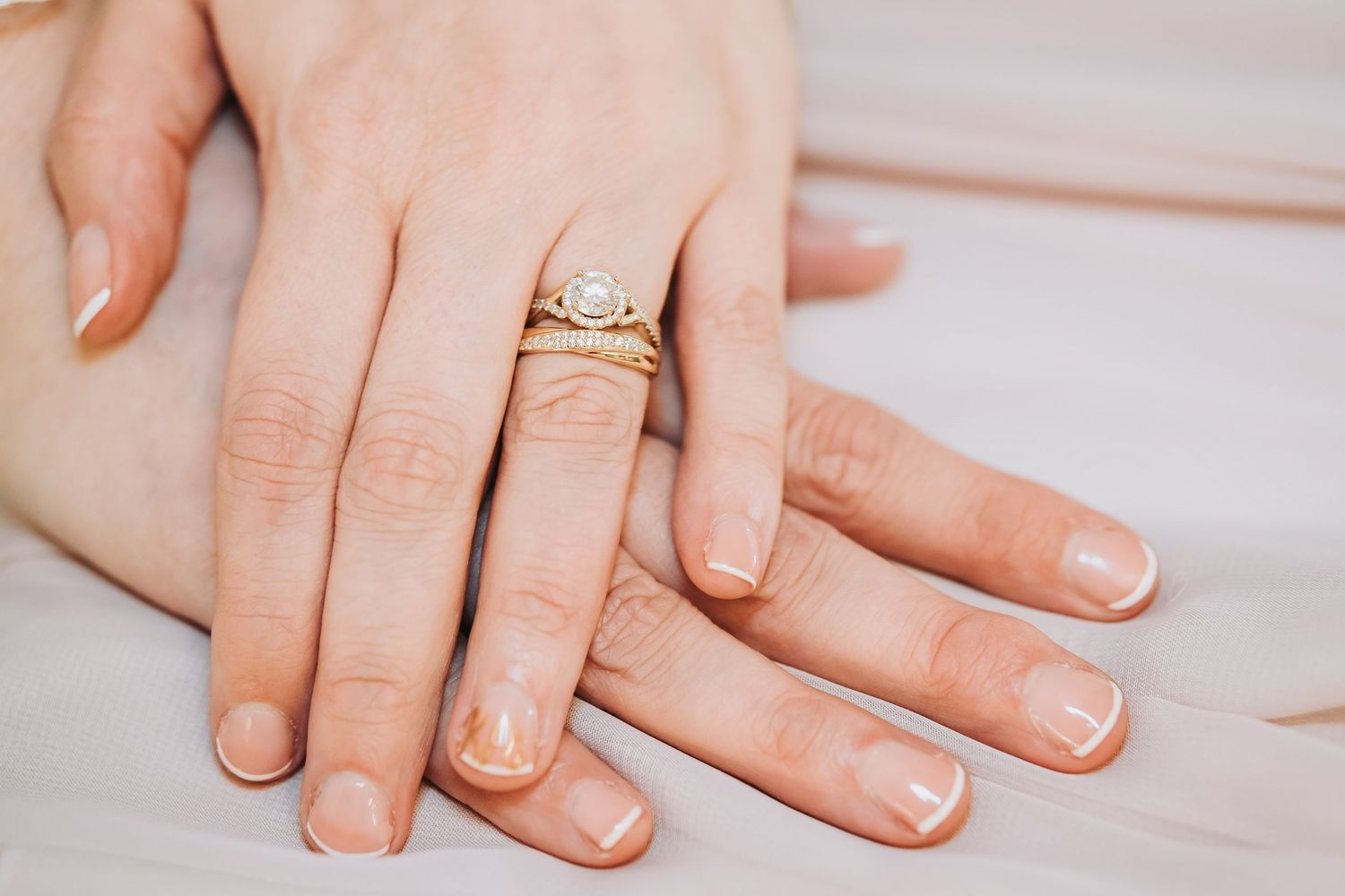 Closeup of hands showing delicate nude nail polish manicure.