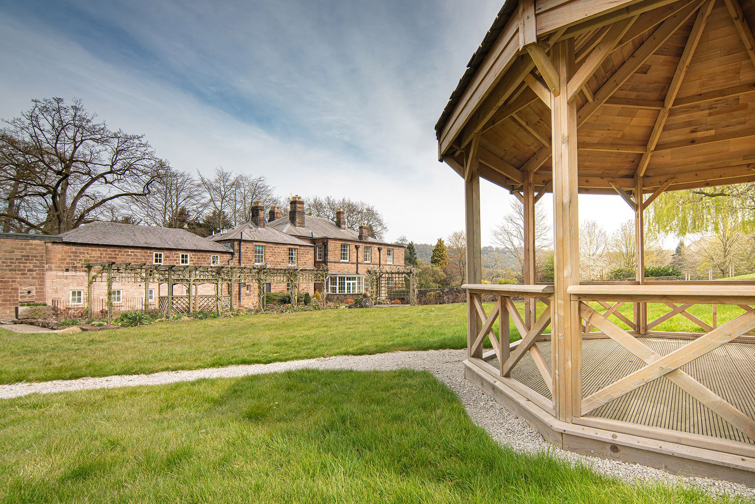 Panoramic view of a rustic wooden gazebo with stone pillars and residential homes in the background during sunset.