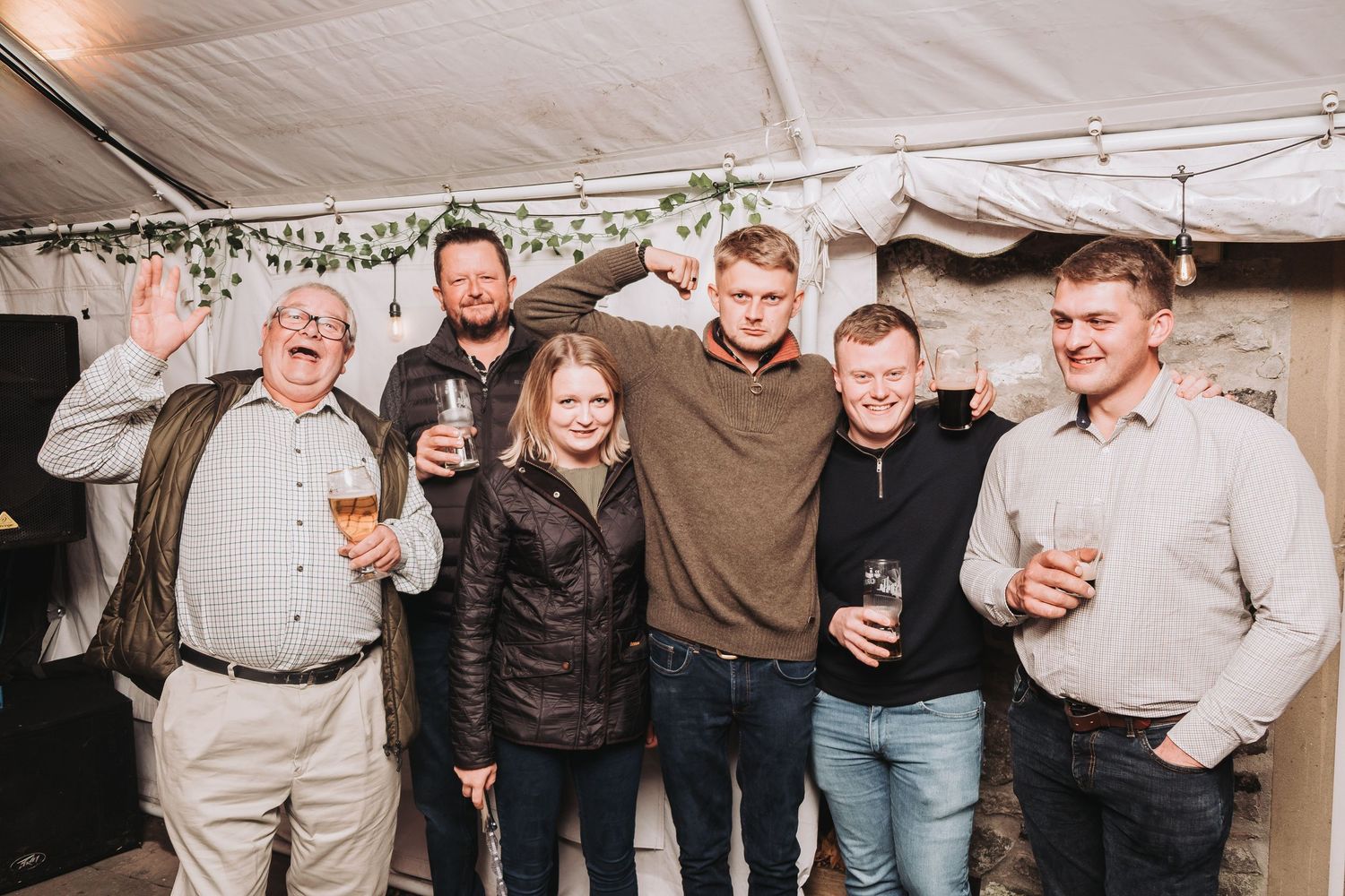 People celebrating and socializing at a lively evening wedding reception under a tent.