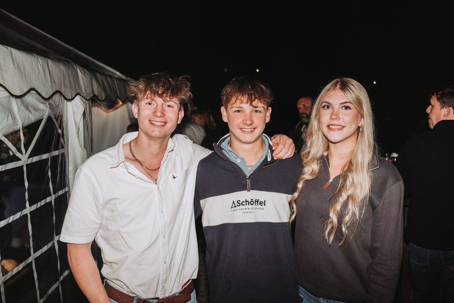 Young friends posing together and smiling at a nighttime event with dark lighting.
