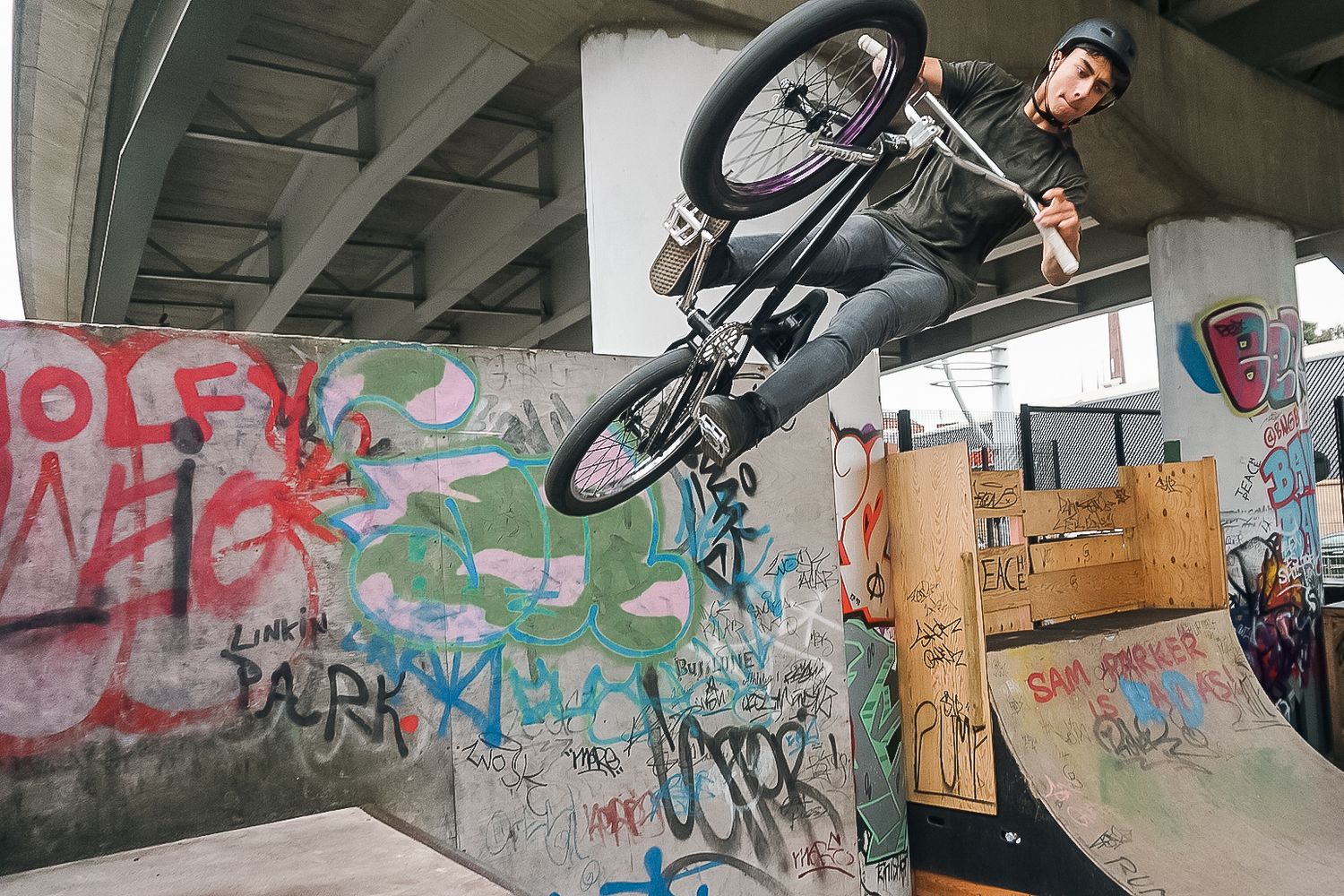 BMX biker executes high jump trick against graffiti-covered wall in urban skate park shot in Leeds by 21 Photography