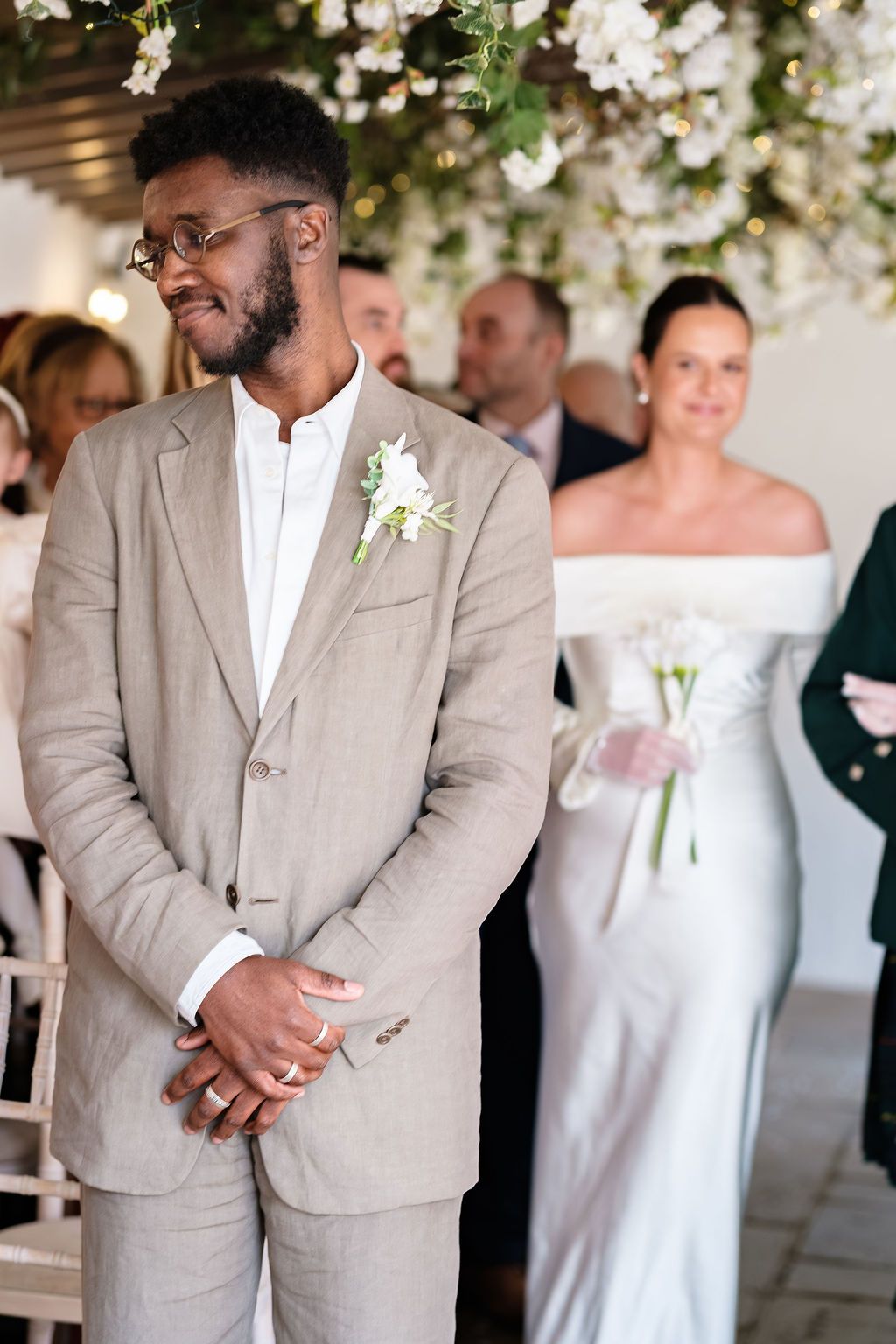 Groom looking over his shoulder at the bride during the ceremony, hanging blossom overhead