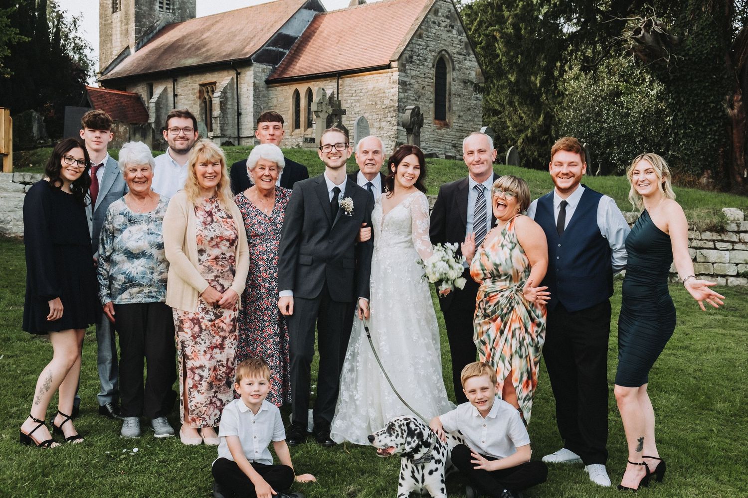 Wedding party poses outdoors for group photos in formal attire with floral dresses and dark suits.