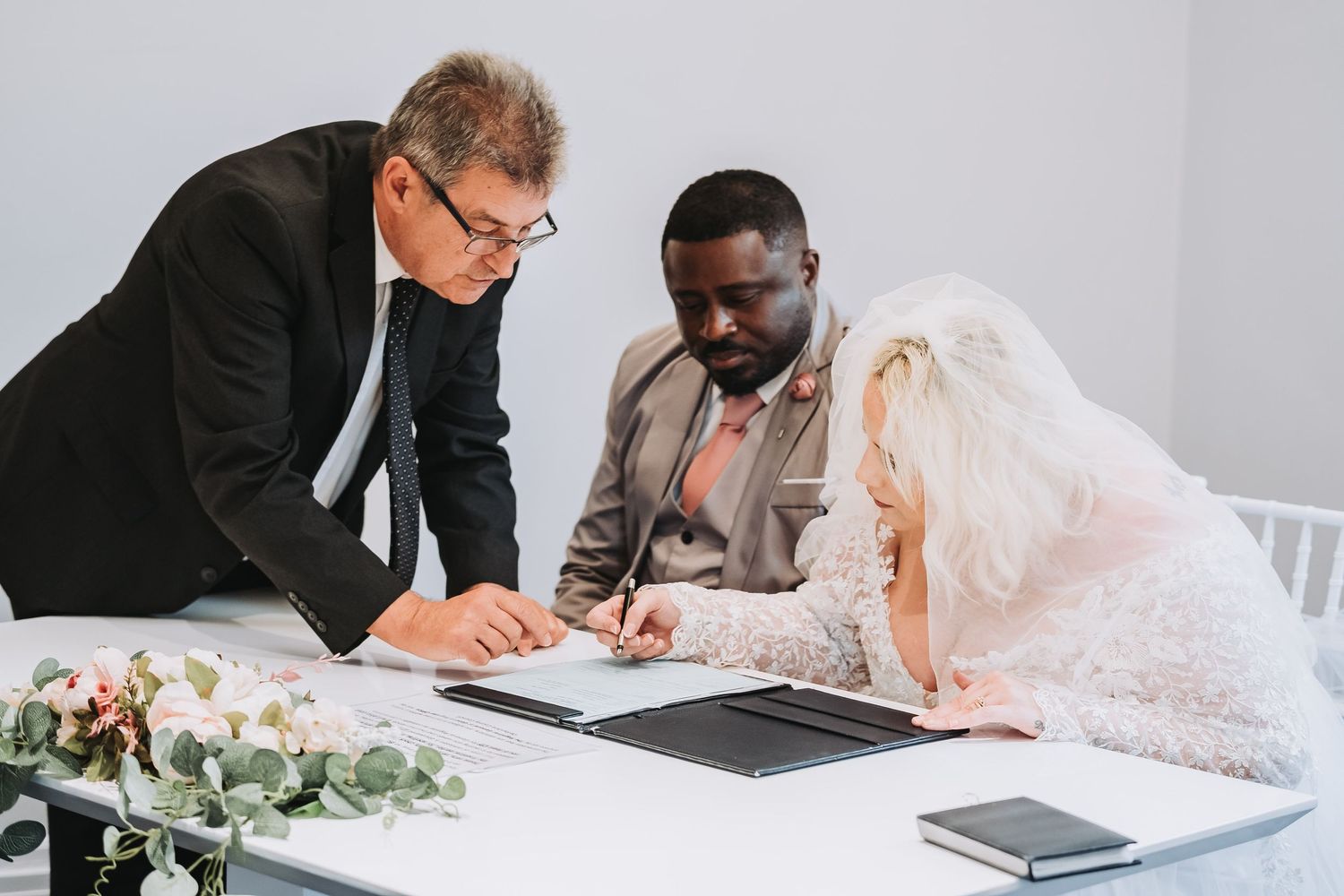Couple signs marriage documents at a table with legal paperwork during civil ceremony.