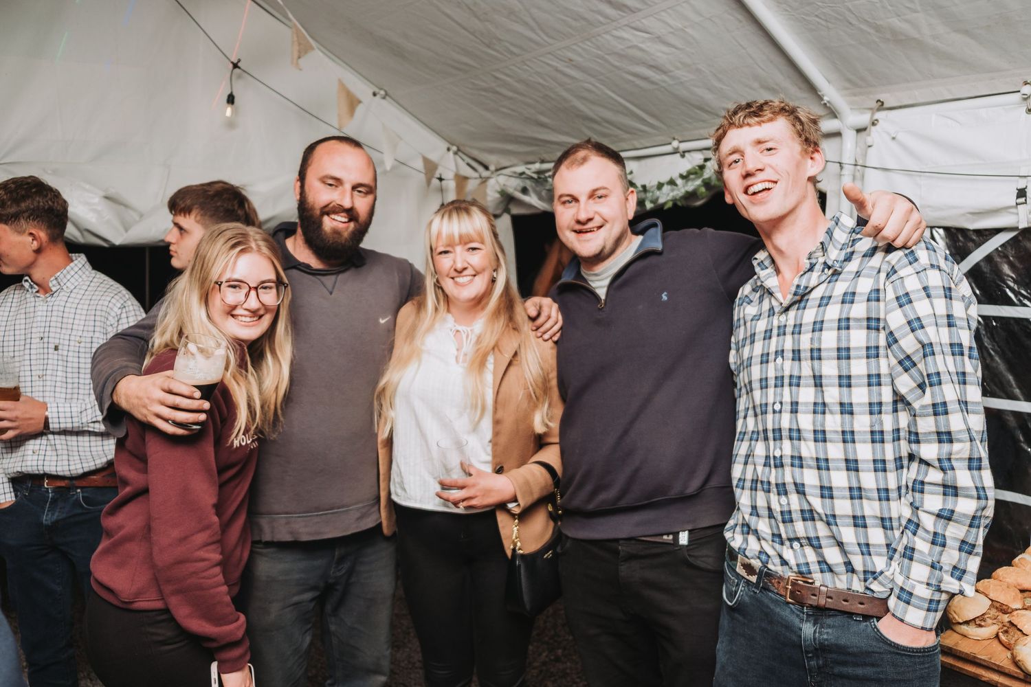 Group of friends laughing together at outdoor event under white tent during social gathering celebration.