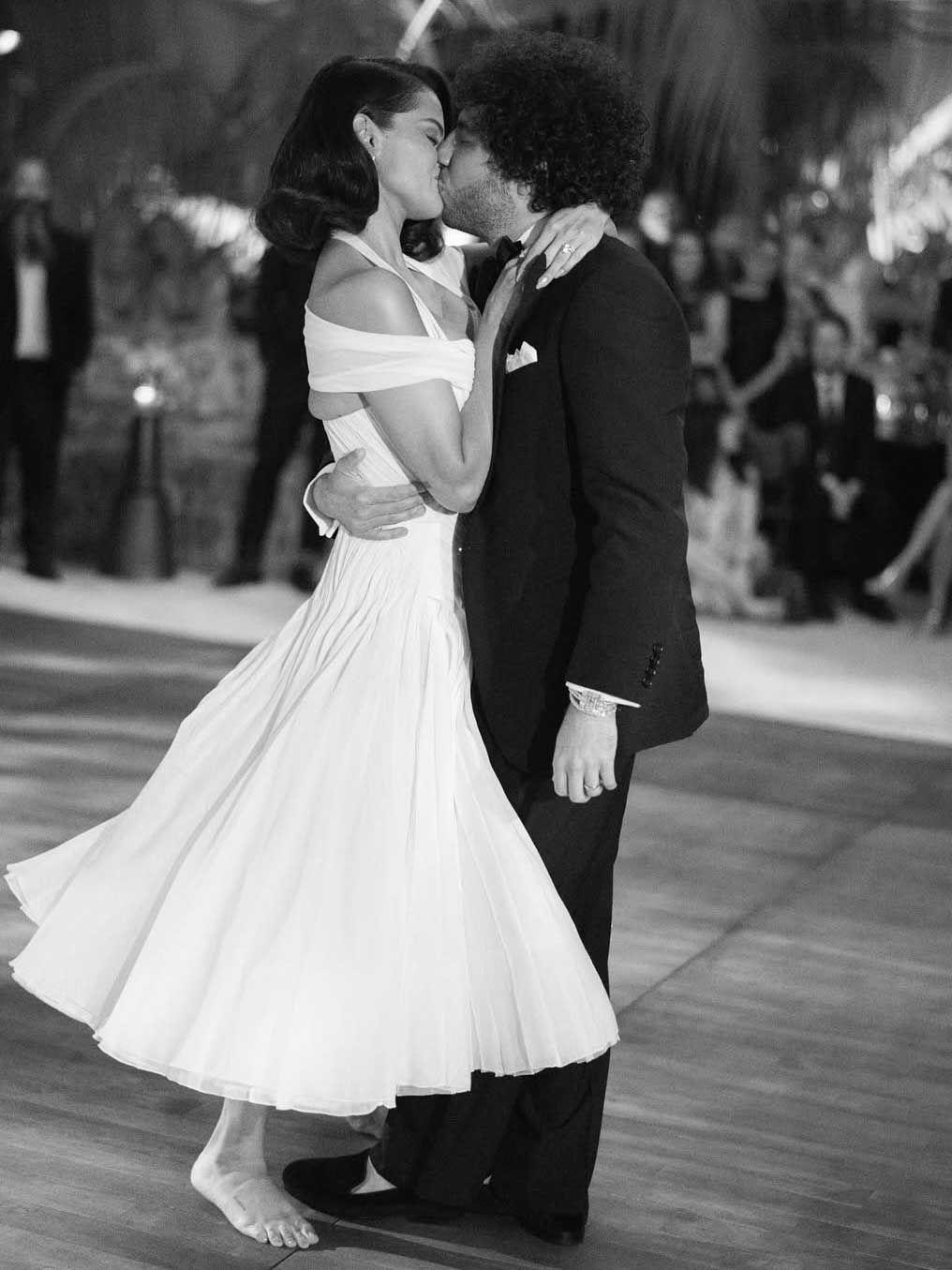 A couple shares an intimate dance moment in black and white, with the bride in an elegant off-shoulder dress and barefoot.