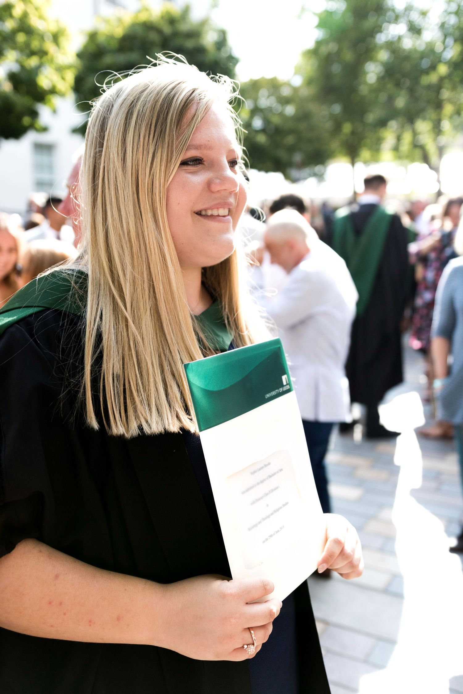 Someone holding a white document outdoors on a sunny day with blurred crowd in background shot in Leeds by 21 Photography
