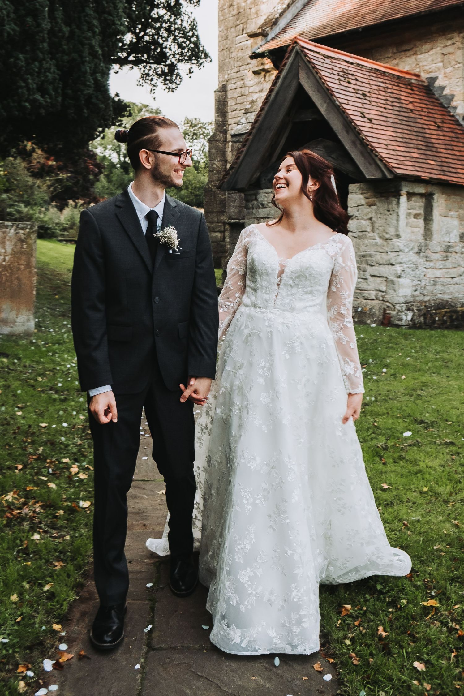 A couple walks together outside a historic stone church on their wedding day.