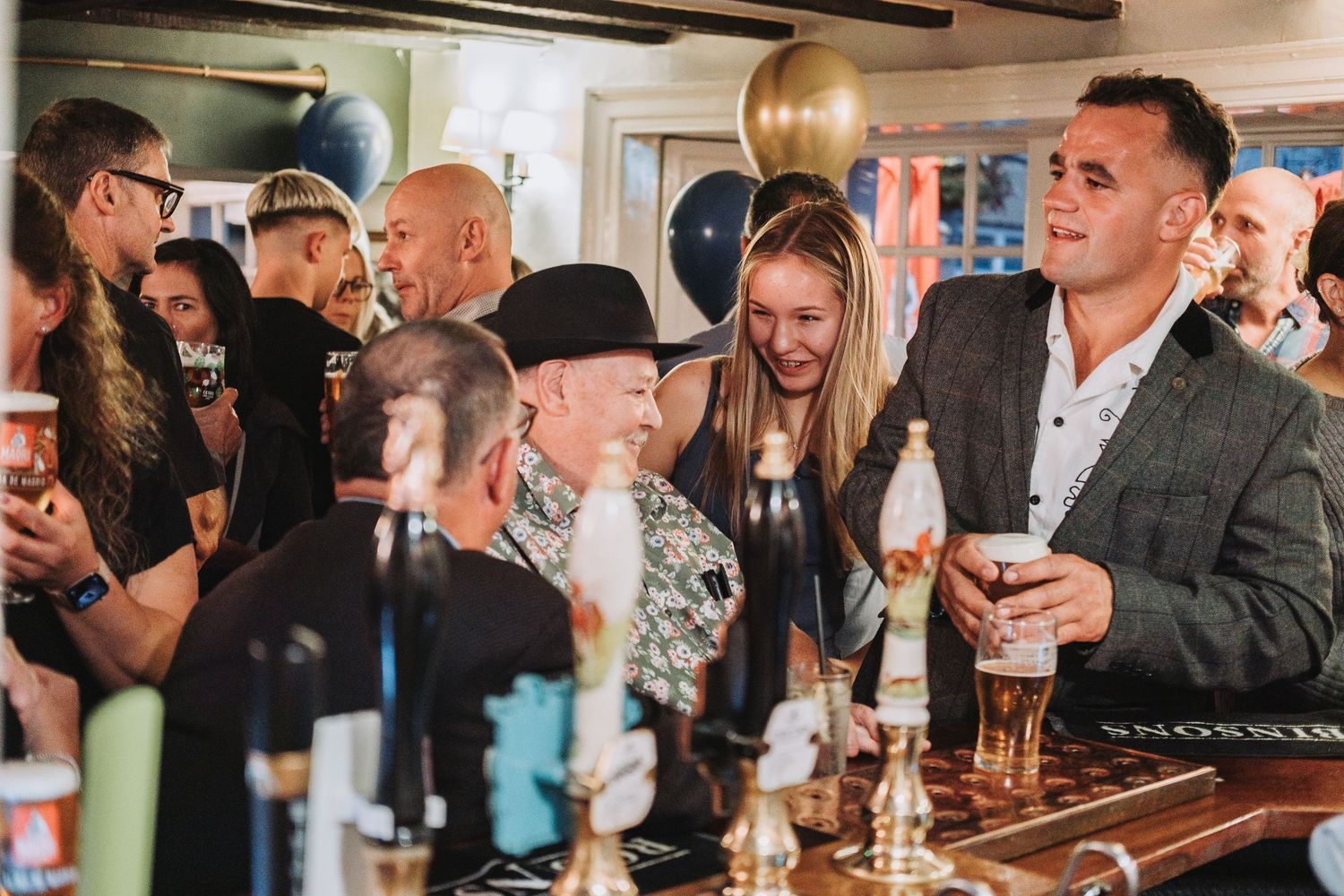 A crowded bar scene with people gathered around drinks in a casual indoor setting.
