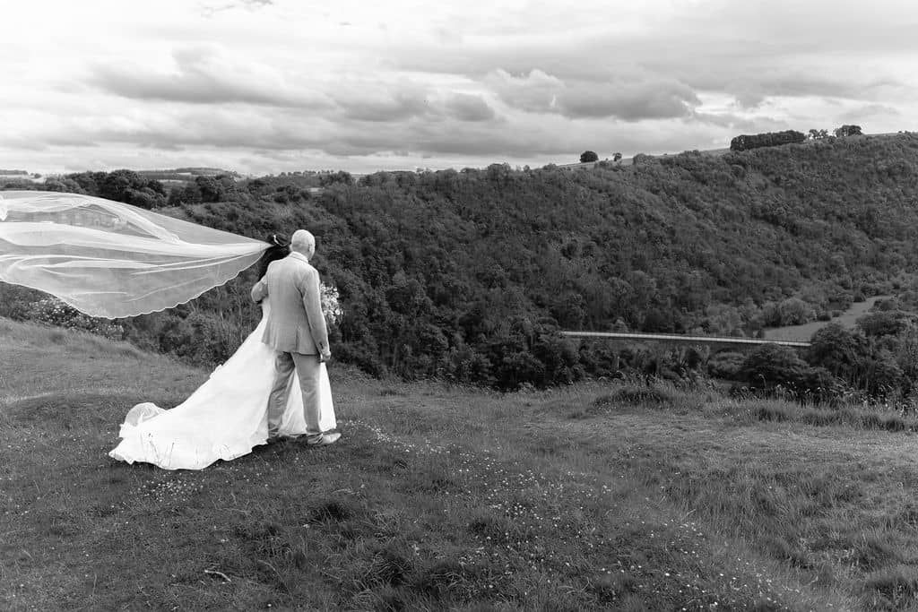 Black and white photo of a bride and groom standing looking at monsal head viaduct taken by 21 photography