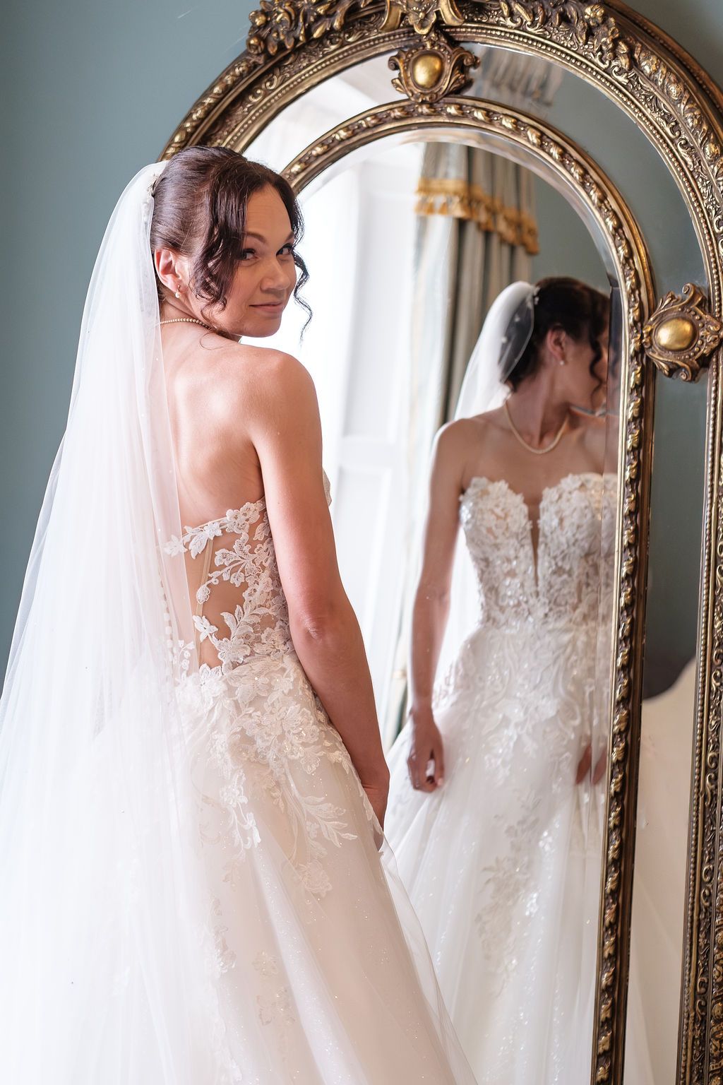 Bride's back and lace dress detail reflected in a gilt mirror, veil visible
