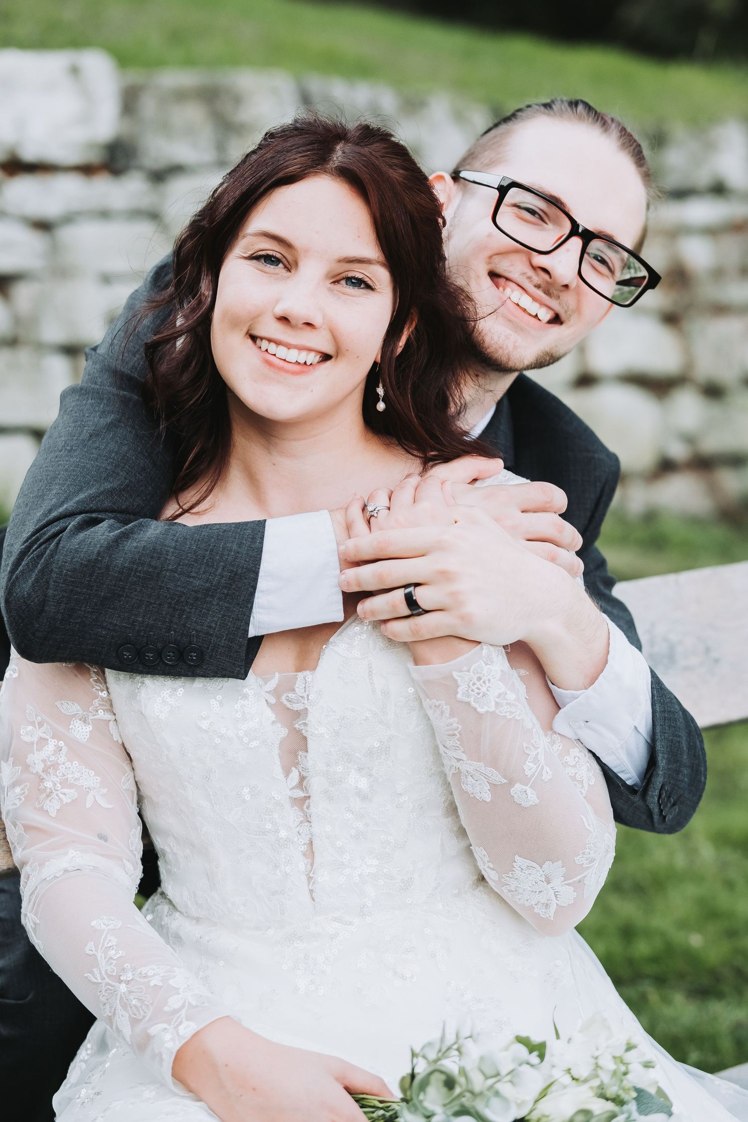 Joyful wedding couple embracing outdoors in front of stone wall.