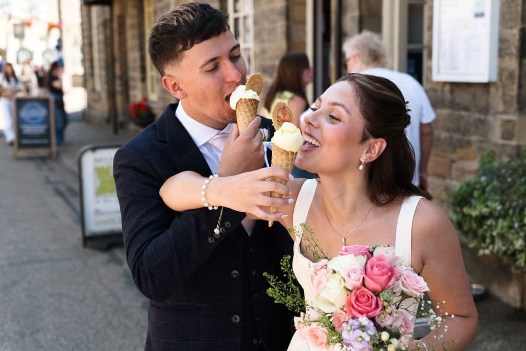 Newlywed couple sharing ice cream cones in Bakewell, bride holding pink bouquet in wedding dress and groom in suit taken by 21 Photography