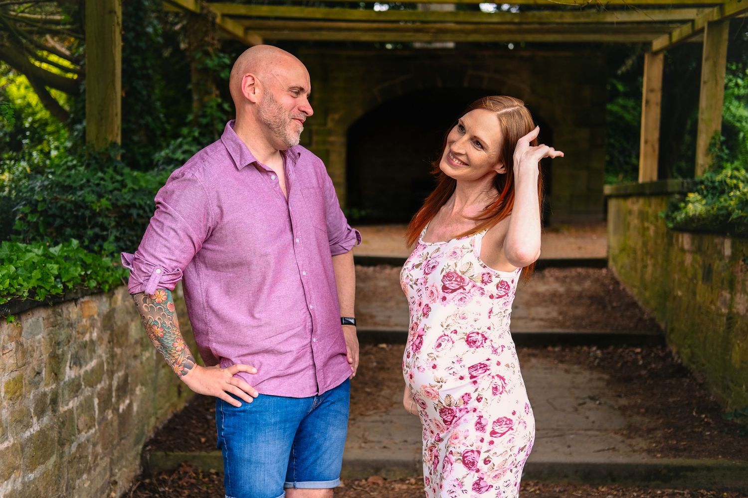 Couple in coordinated pink outfits posing under a shaded stone archway.