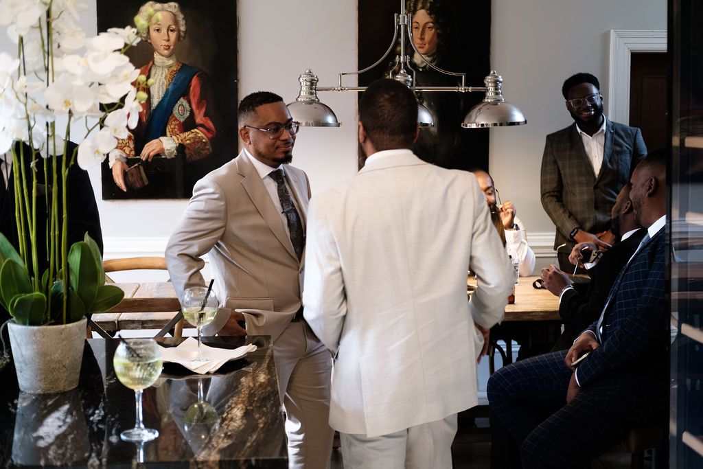 Groomsmen talking over drinks in a room with orchids and gallery paintings