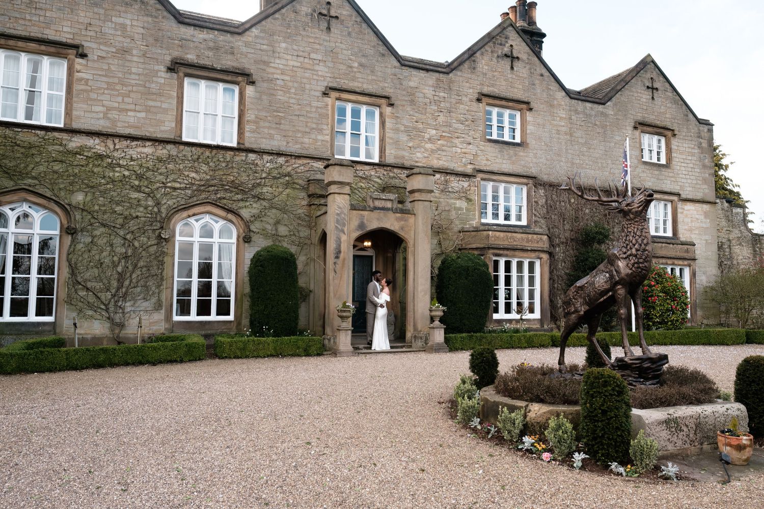 Full facade of Dunston Hall with the bronze stag statue and couple in the doorway
