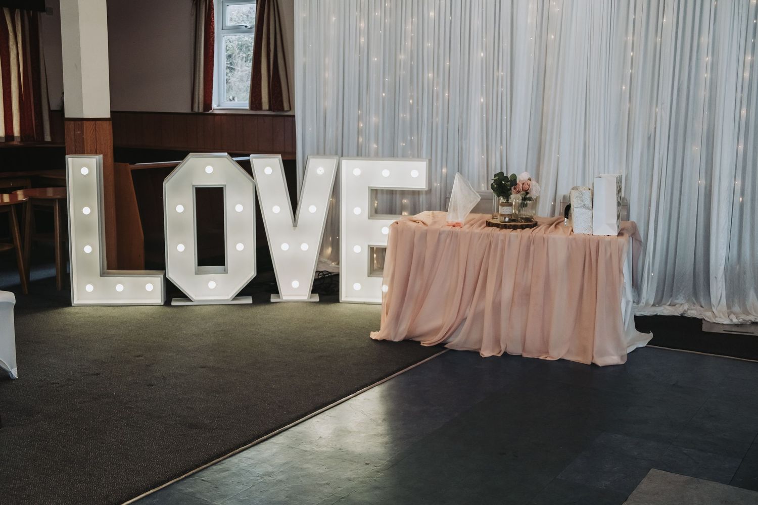 Wedding reception venue decorated with white drapes and romantic lighting showcases tables and LOVE sign backdrop.