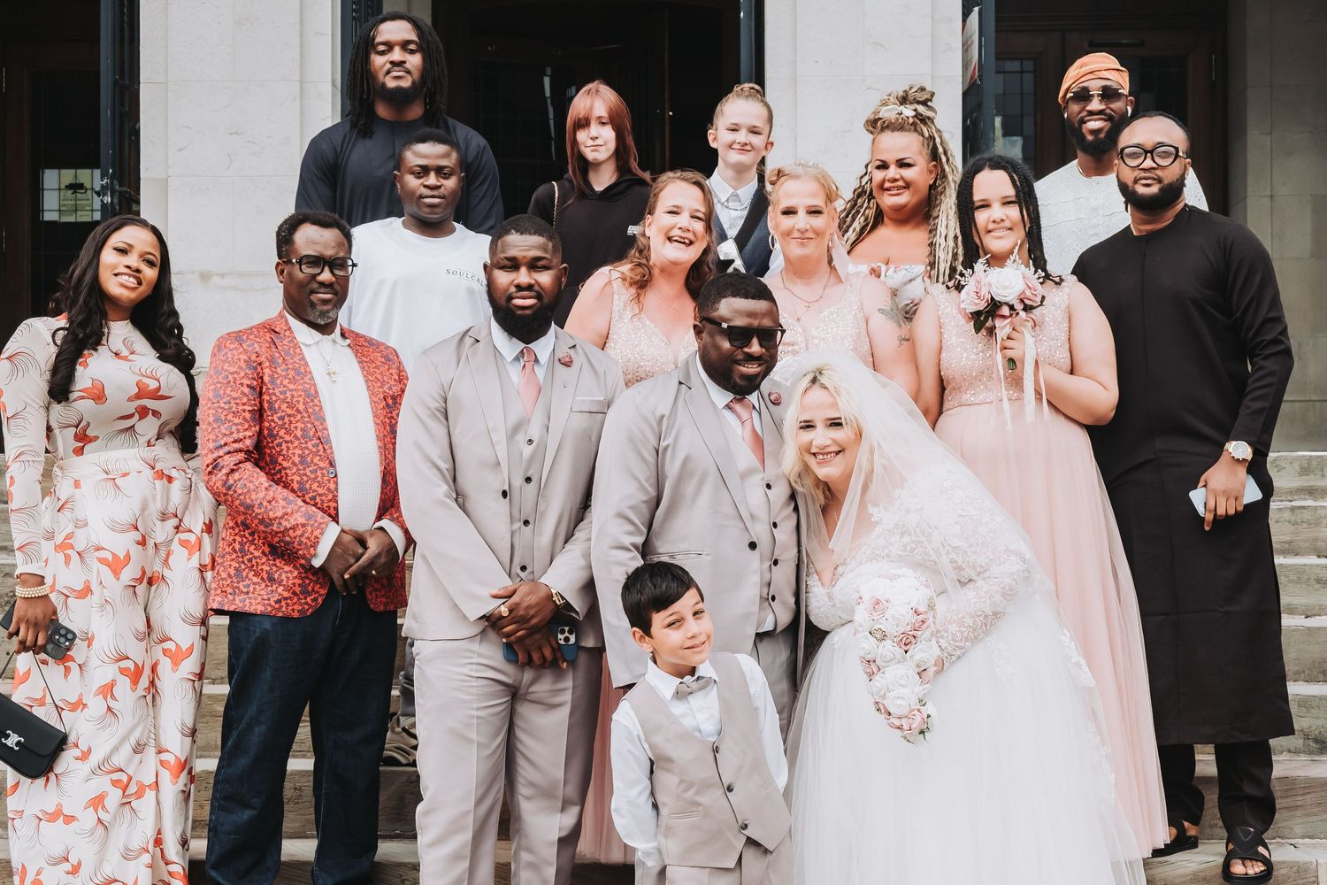 Wedding party poses together outside in coordinated coral and floral outfits.