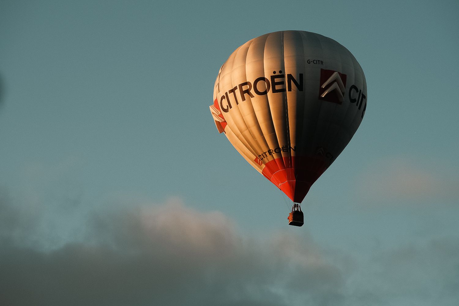 A Citroën branded hot air balloon soaring against a blue sky with soft clouds below.