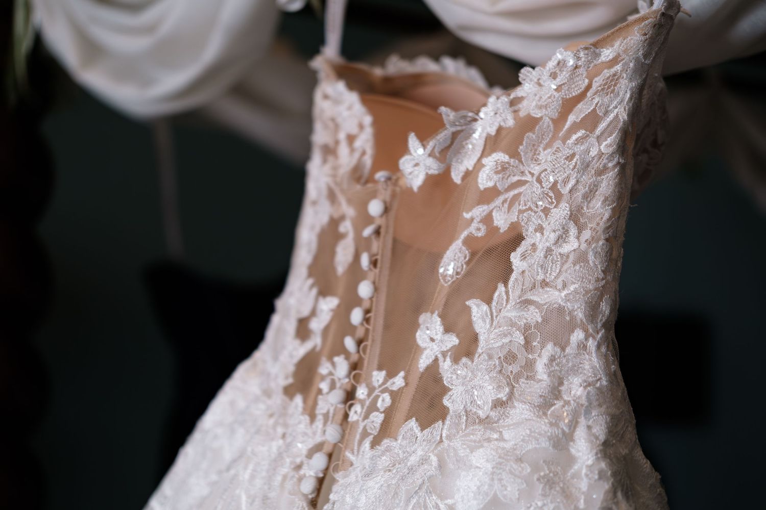 Close-up of a bridal gown featuring intricate lace floral appliqués and delicate button-up corset back detailing.