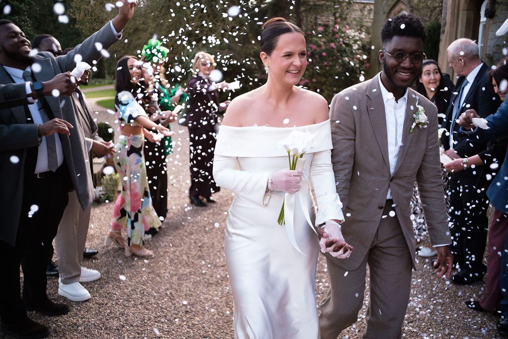 Couple walking through confetti outside, bride in a fitted white dress